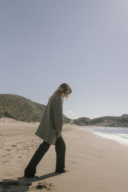 A woman walks along a serene beach, showcasing casual and elegant fashion. Perfect for lifestyle topics.