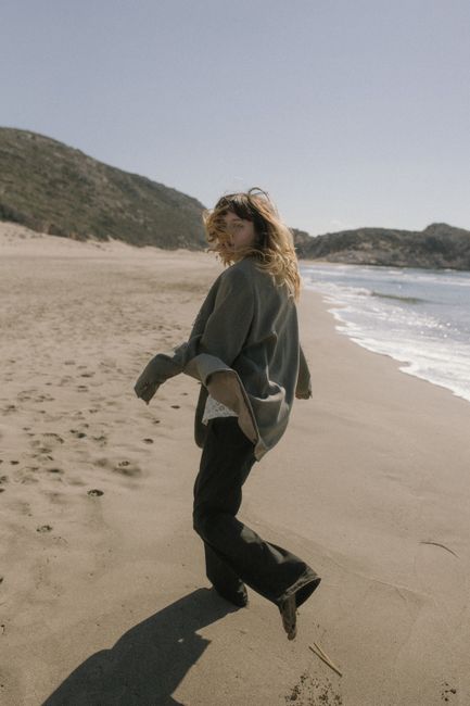 A woman running joyfully along a deserted beach on a sunny day with hills in the background.