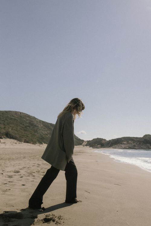 Free A fashionable woman strolls on a sunlit beach, blending elegance with nature. Stock Photo