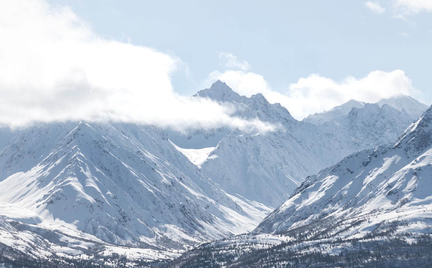 Snow-covered mountain peaks in Alaska with cloud drifting across the summits