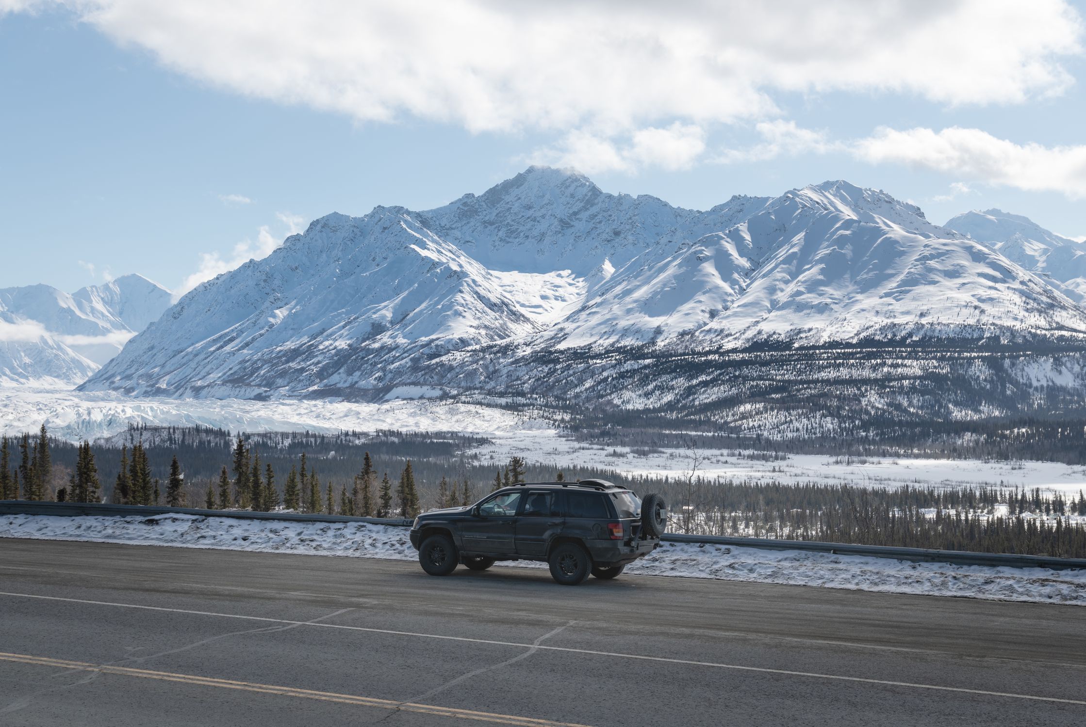 4x4 vehicle on a snowy road with mountainous backdrop in Alaska during winter.