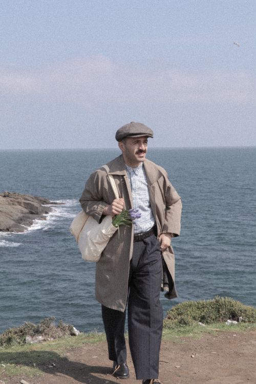 Free A man in retro attire with a satchel walks along the seashore on a sunny day. Stock Photo