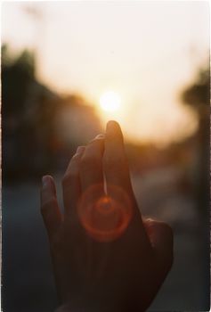 A hand reaches for the setting sun, casting a warm glow in an outdoor scene.
