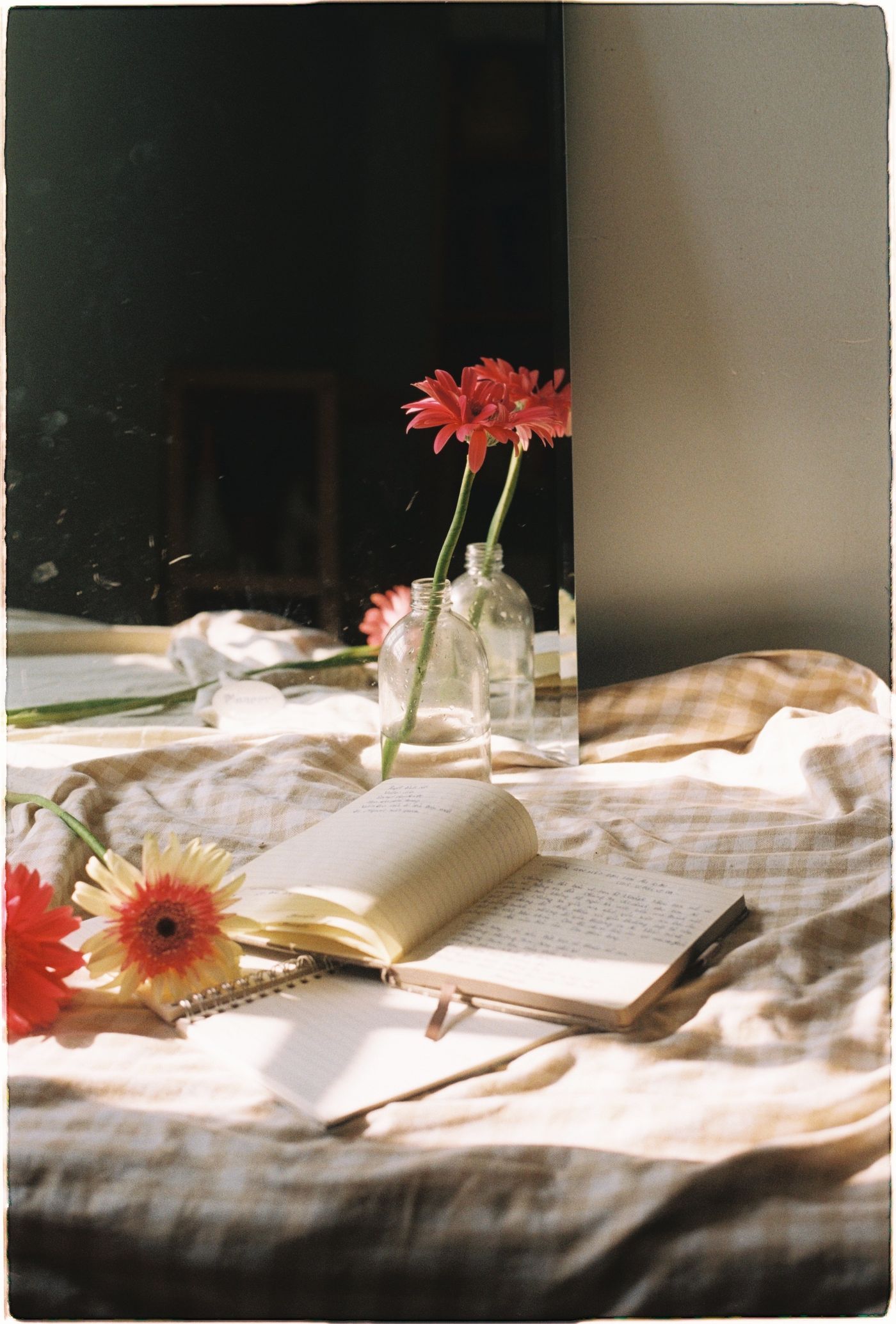 Open book, flowers and a notebook resting on a bed