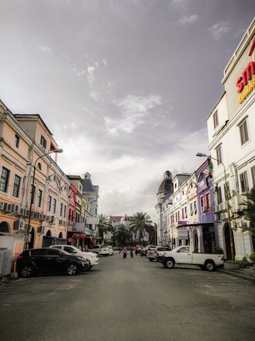 Free Urban street with classic architecture, parked cars, and vibrant colors under a cloudy sky. Stock Photo