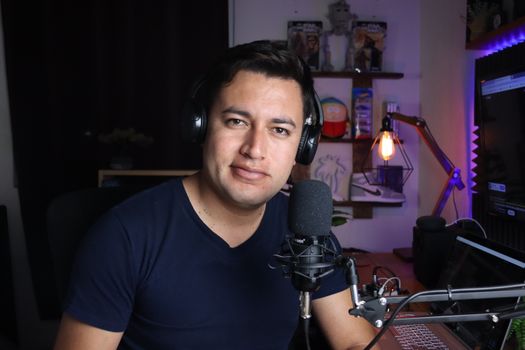 Portrait of a male podcaster in a home studio with microphone and headphones.