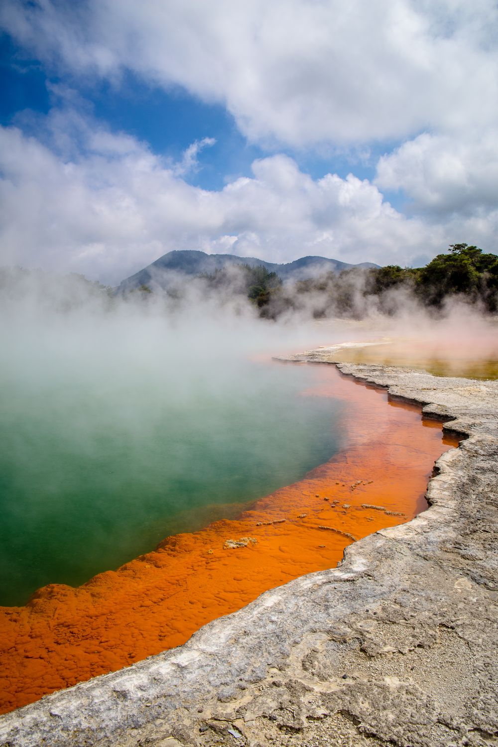 Detalle del borde anaranjado de Champagne Pool curvándose entre vapor y aguas verdosas