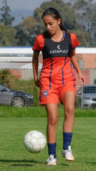 Female soccer player practicing on a sunny day. Wearing orange uniform and sports vest.