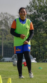 A woman in sports gear smiling during soccer practice on a sunny outdoor field.
