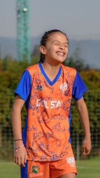Young girl soccer player smiling with eyes closed in vibrant uniform outdoors.