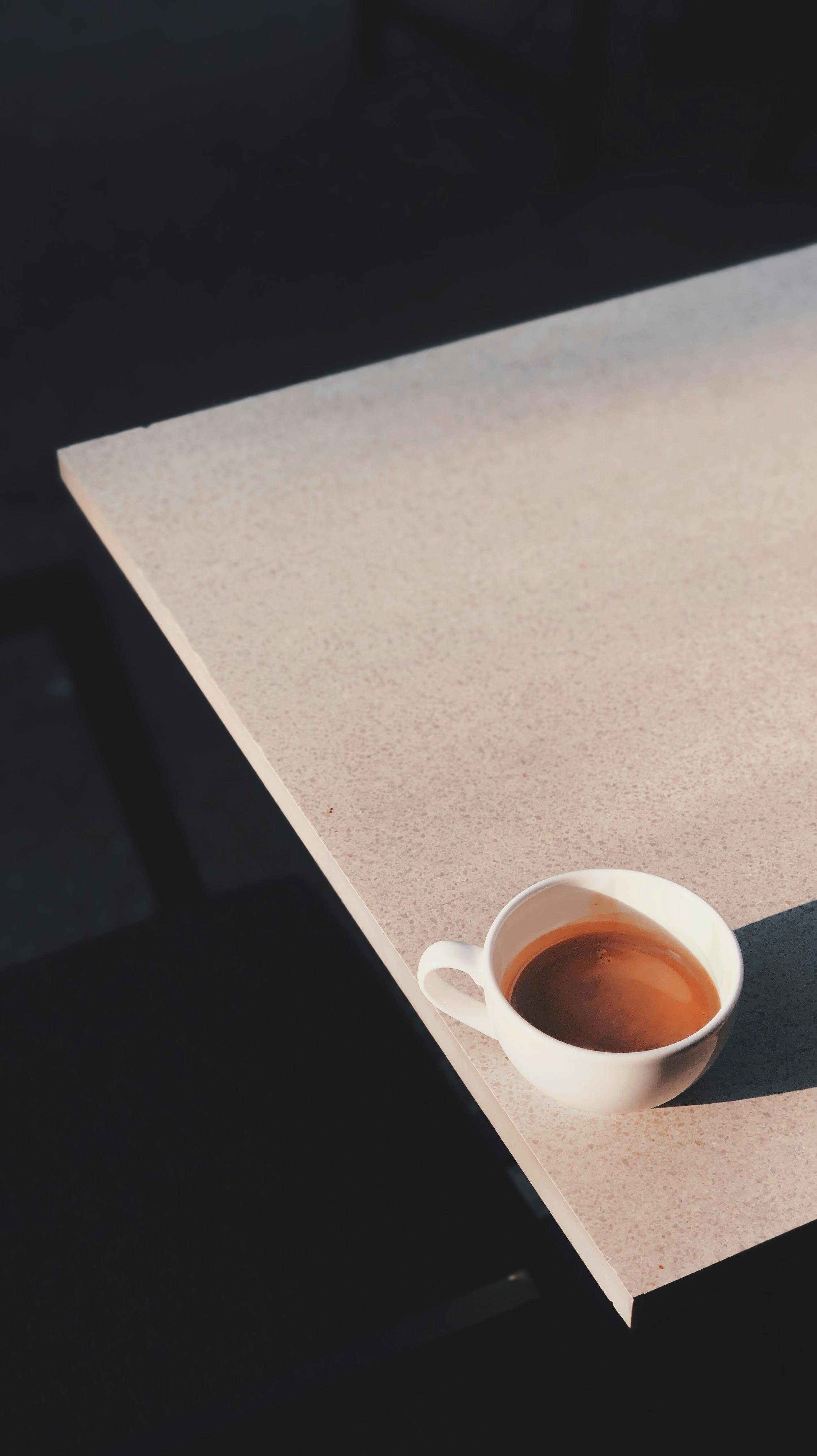 A simple white coffee cup casting a shadow on a sunlit table, exemplifying minimalist design.
