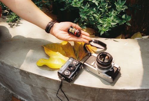 Hand Holding Photographic Film over Vintage Cameras
