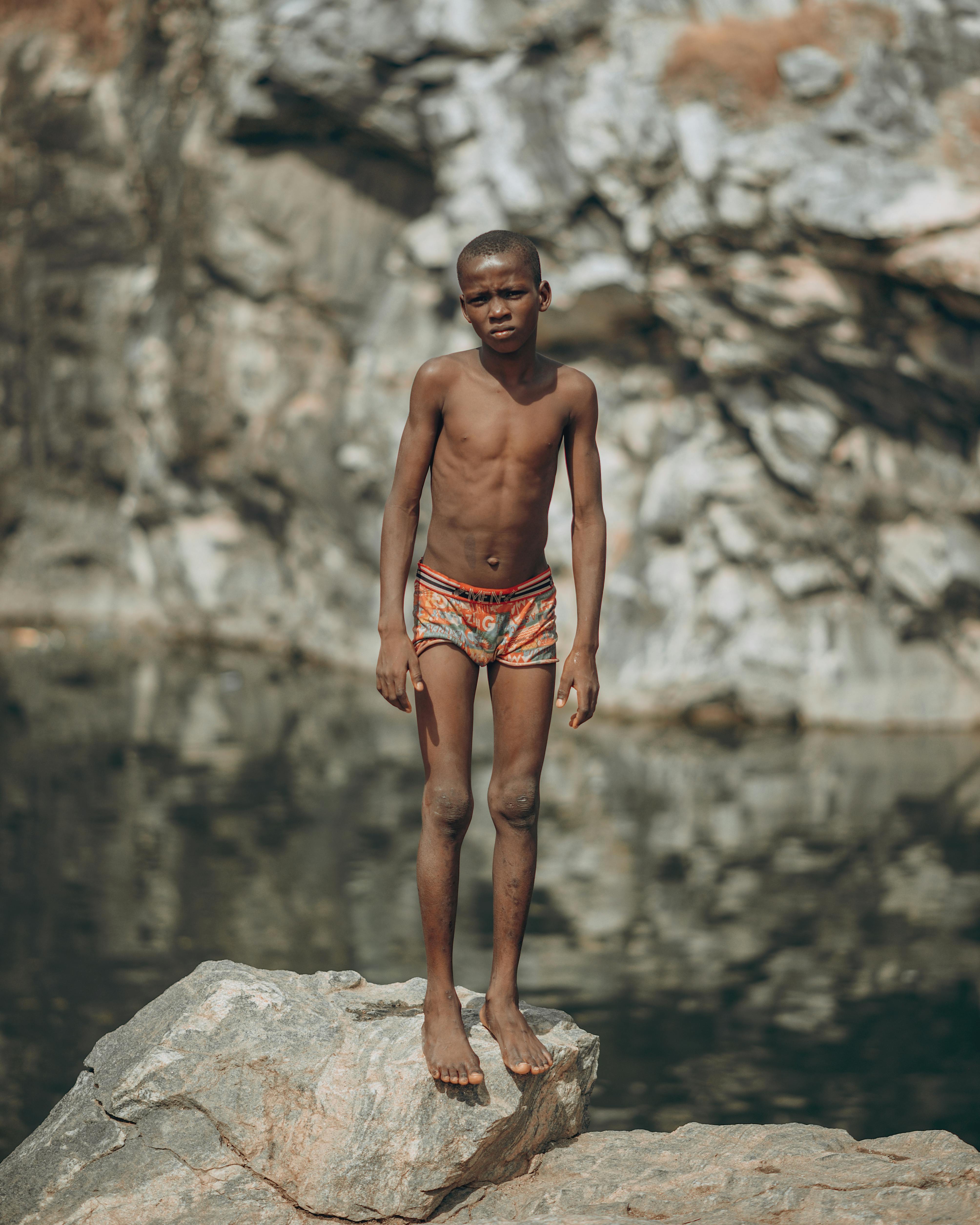 Boy in Underwear Standing on Rock over Lake Free Stock Photo