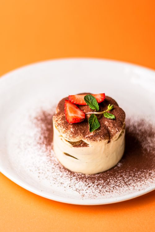 Free Close-up of a classic tiramisu topped with strawberries and mint on an orange background. Stock Photo