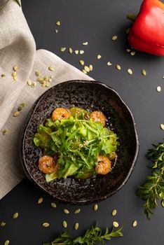 High-angle shot of a shrimp and arugula salad in a rustic bowl with a dark background.