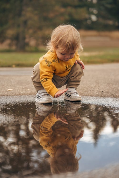 Blond Baby Girl Playing with a Puddle in a Park