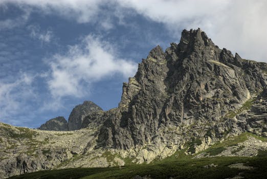 Dramatic rocky mountain peak under a vibrant blue sky with fluffy clouds. Ideal for nature enthusiasts.