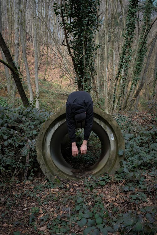 A Man Leaning over a Concrete Crawl Tunnel in the Forest 