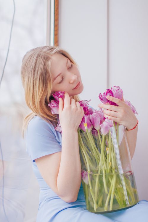 Free Peaceful moment of a woman holding pink tulips seated by a window. Stock Photo