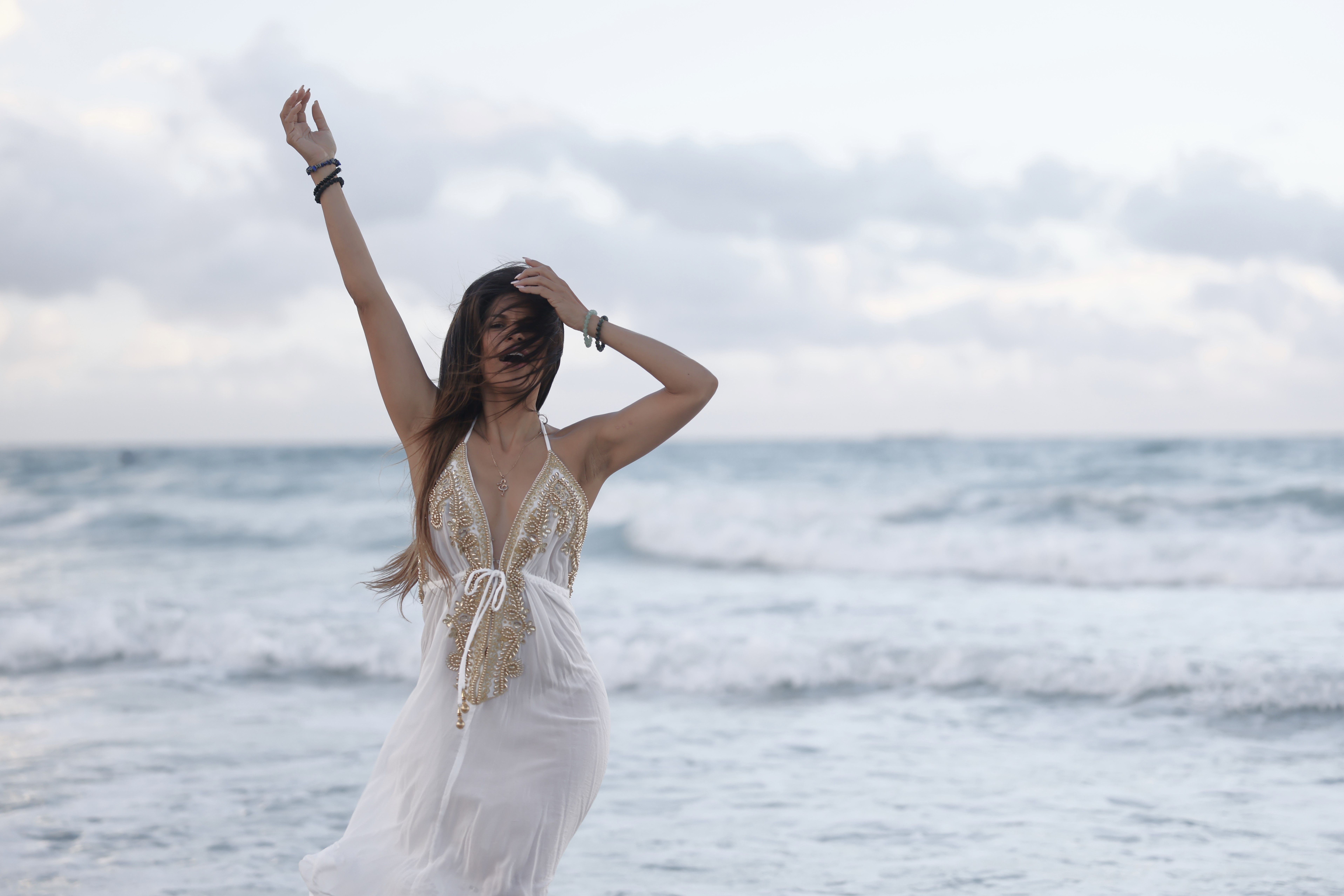 Young Brunette in a White Dress Standing on the Beach with Arm Raised ...