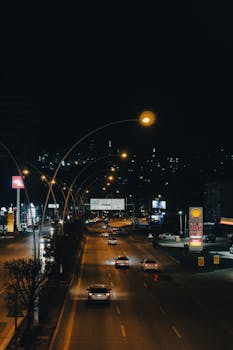 A city highway at night with cars moving under illuminated streetlights, showcasing urban nightlife and transportation.