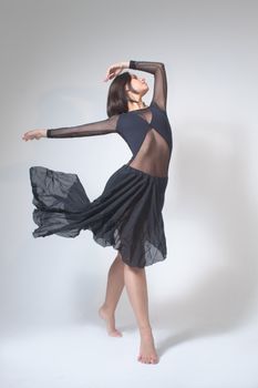 Ballet dancer performing a graceful pose in a studio with a flowing black dress and barefooted motion.