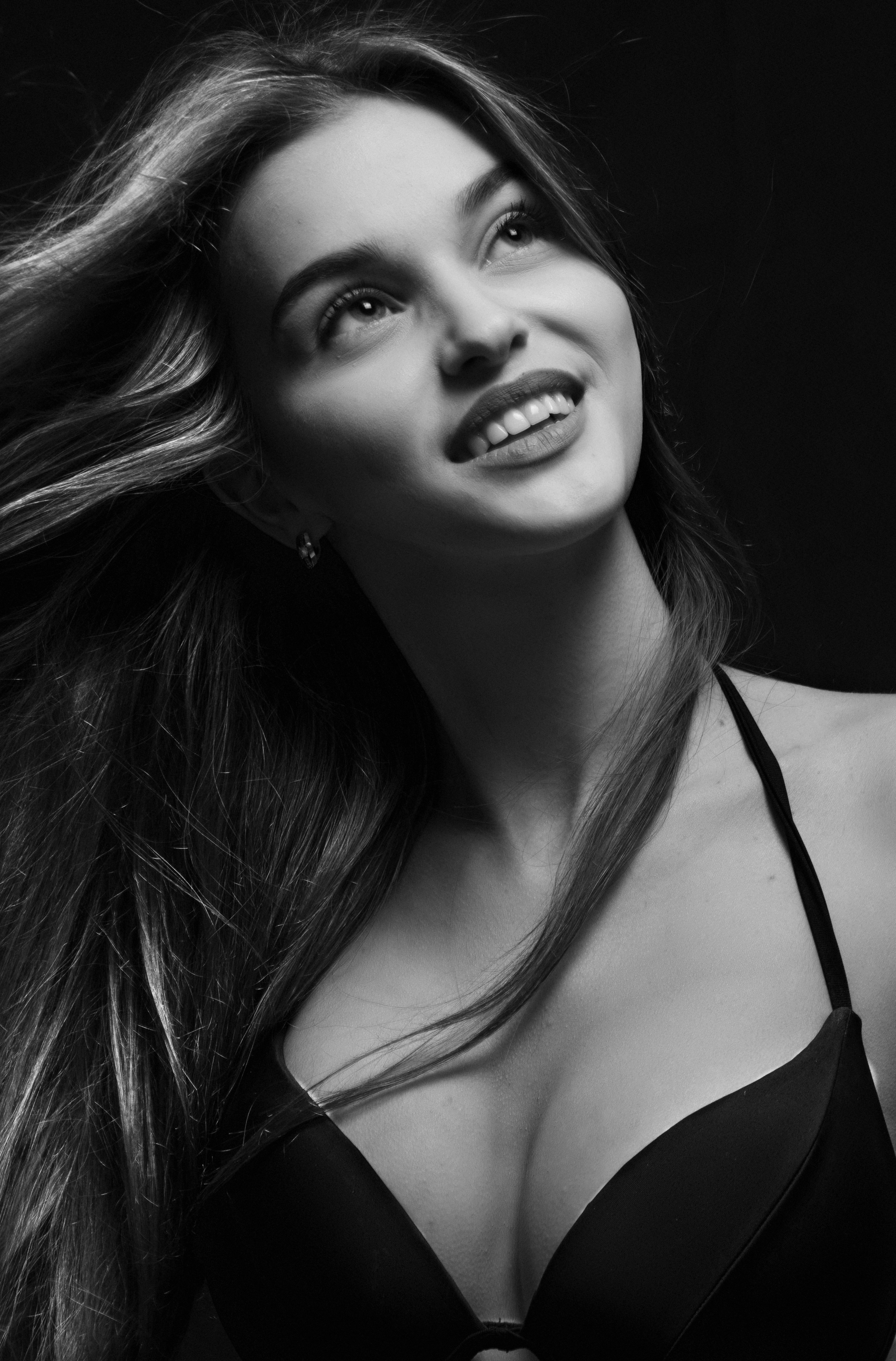 A captivating black and white portrait featuring a smiling woman looking upward against a dark background.