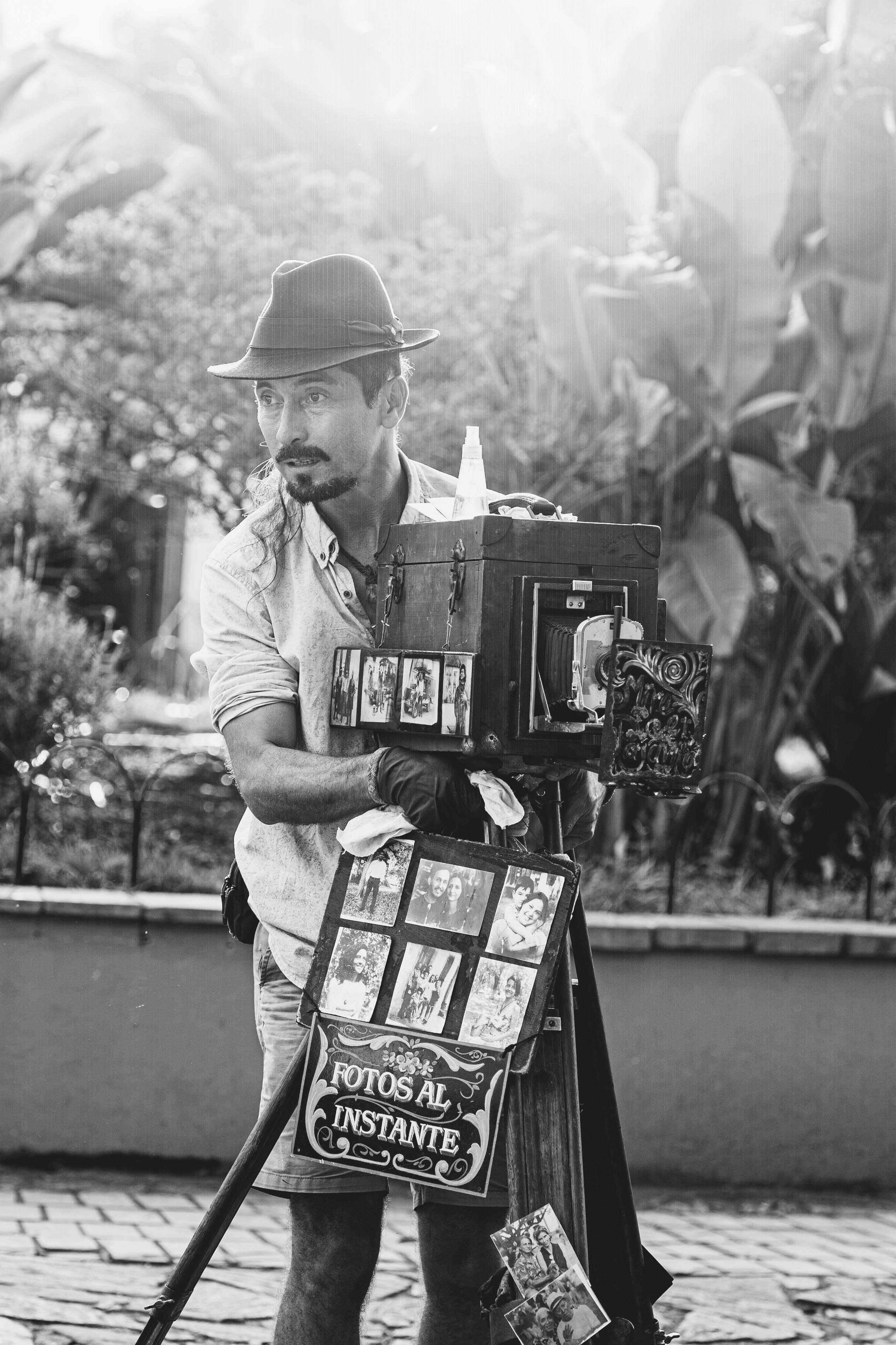 Black and white image of a street photographer with an antique camera showcasing instant photos.