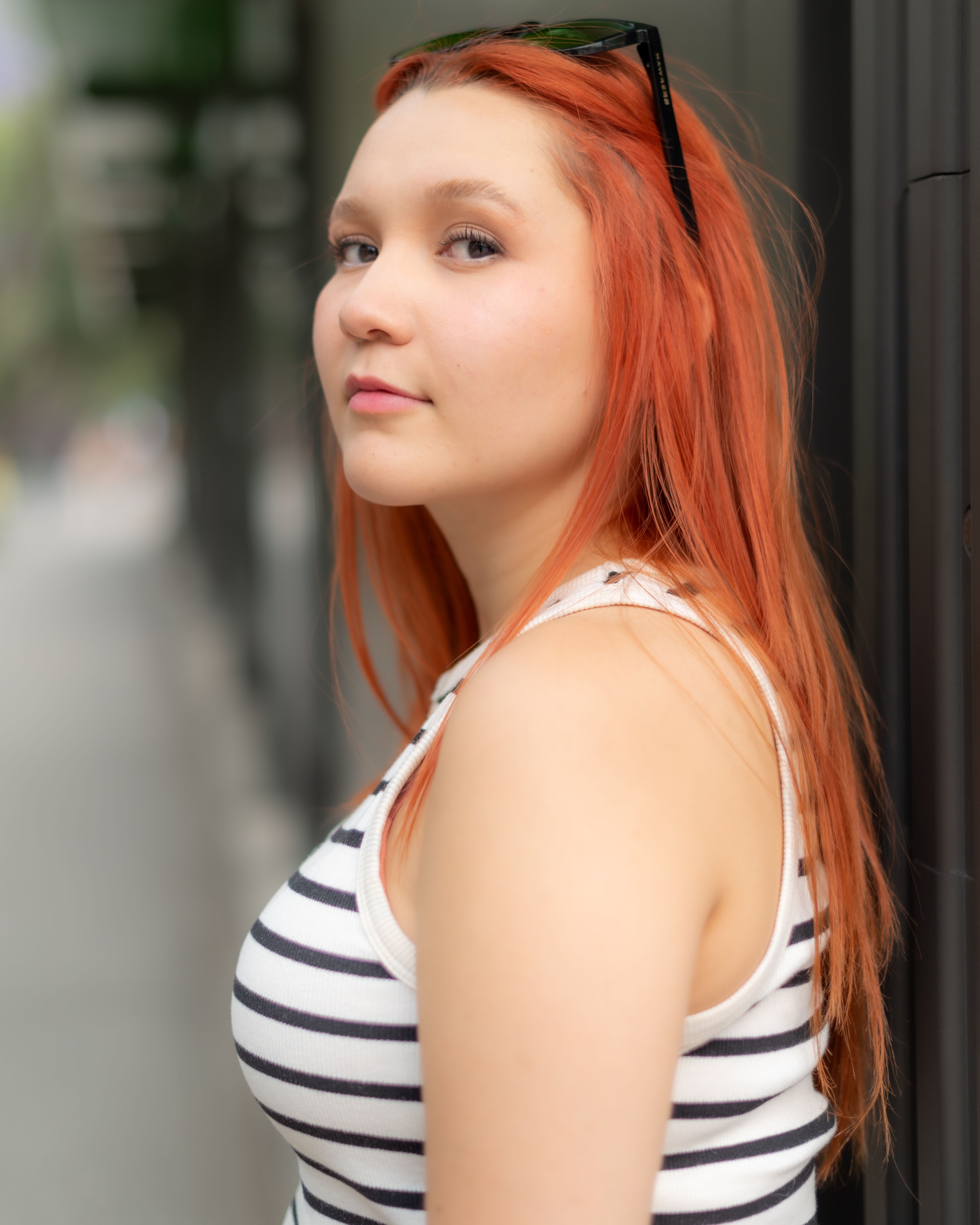 A striking portrait of a redhead woman posing confidently in an urban outdoor setting.