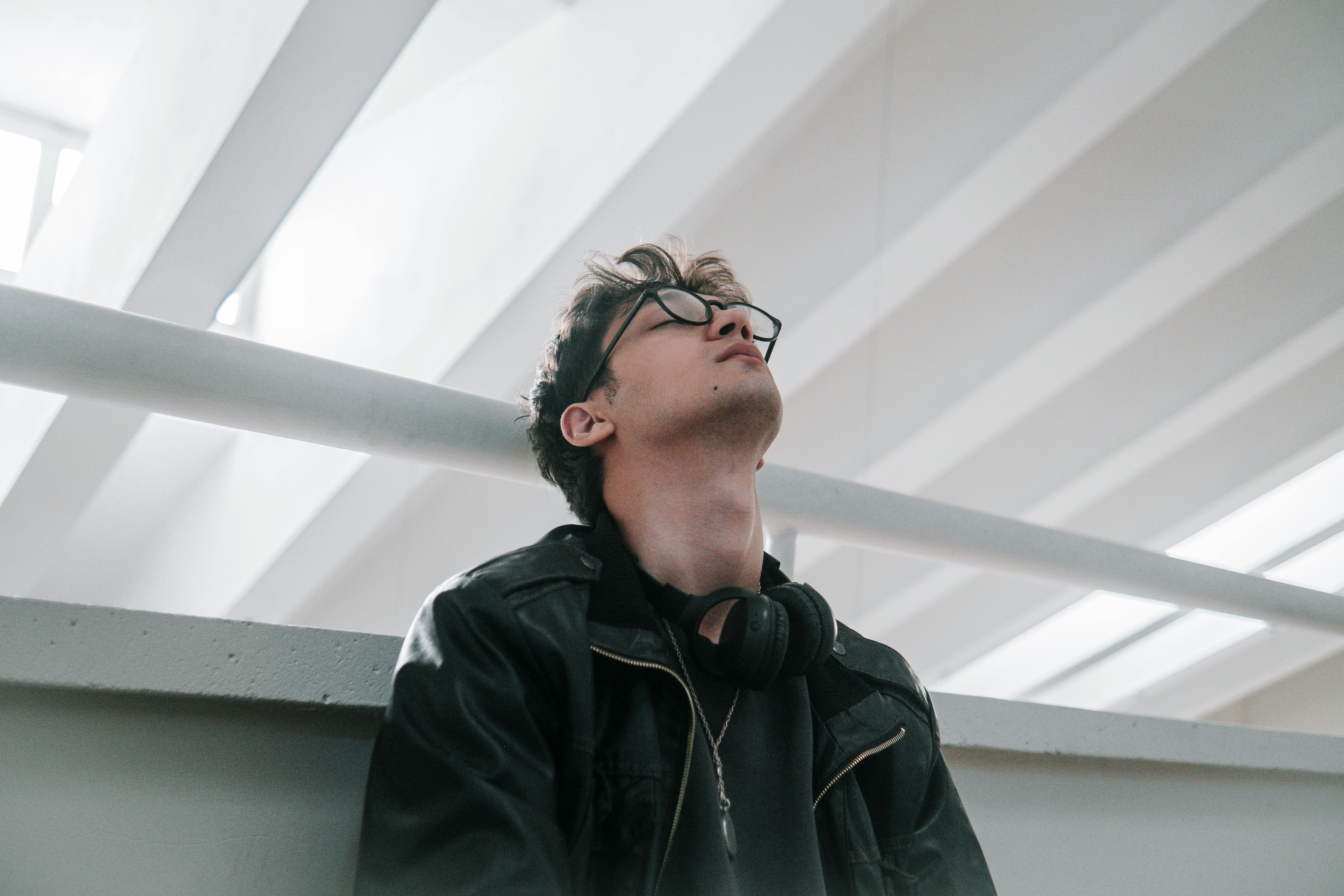 Stylish young man in an urban setting wearing a leather jacket and eyeglasses.