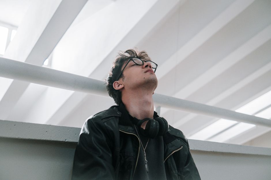 Stylish young man in an urban setting wearing a leather jacket and eyeglasses.