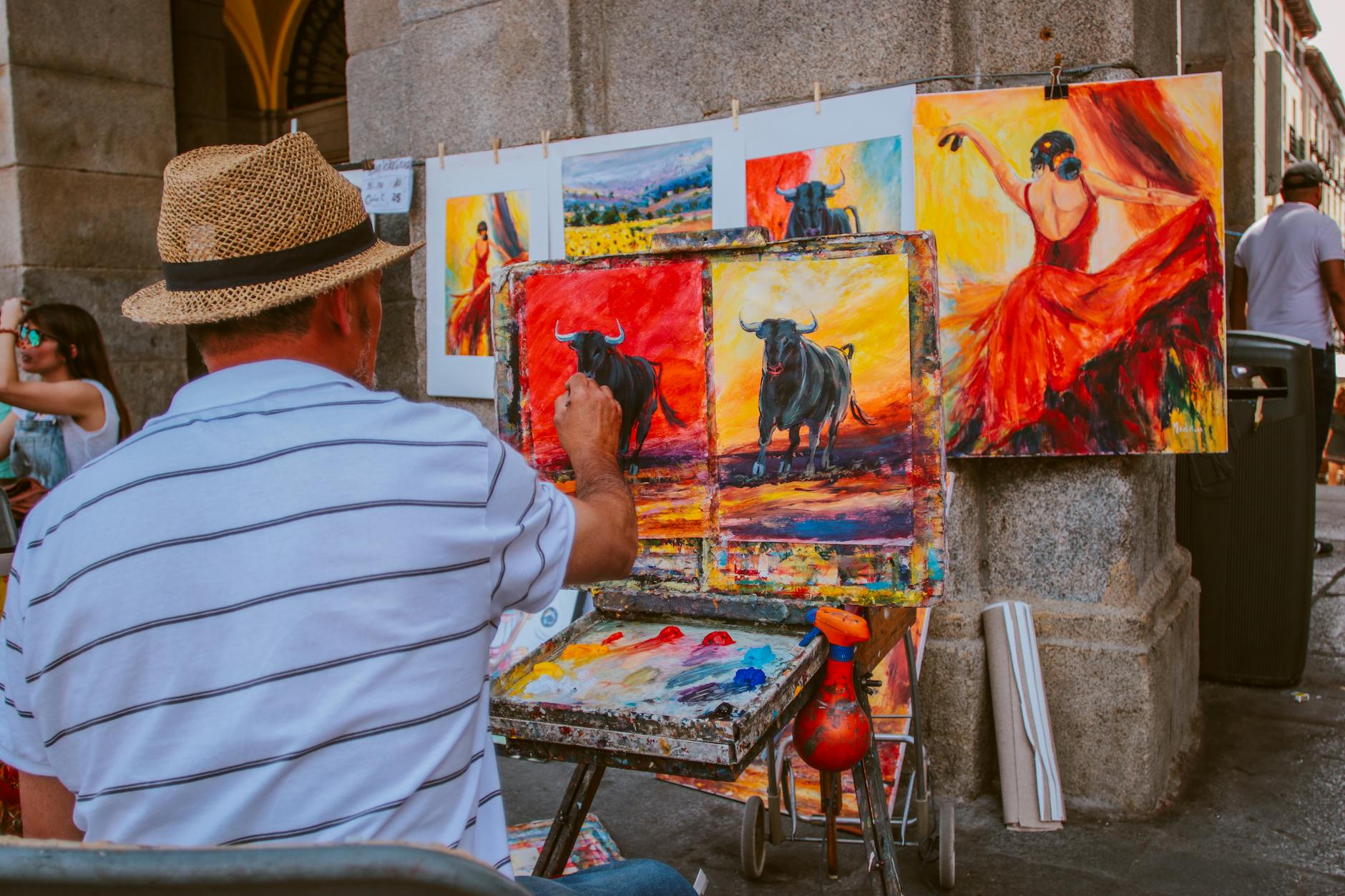Street artist painting vibrant bull and flamenco dancer scenes in an outdoor market.
