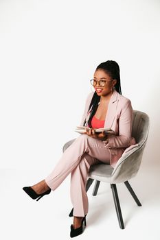 Confident woman in a pink suit posing with a book and smiling, set against a white background.