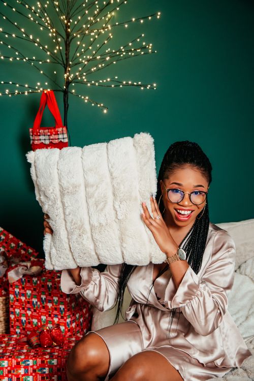 Free Woman in festive attire holding gift pillow in cozy Christmas setting. Stock Photo