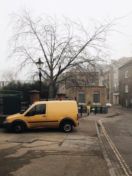 在伦敦一条雾蒙蒙的街道上，一辆黄色货车停在鹅卵石路上