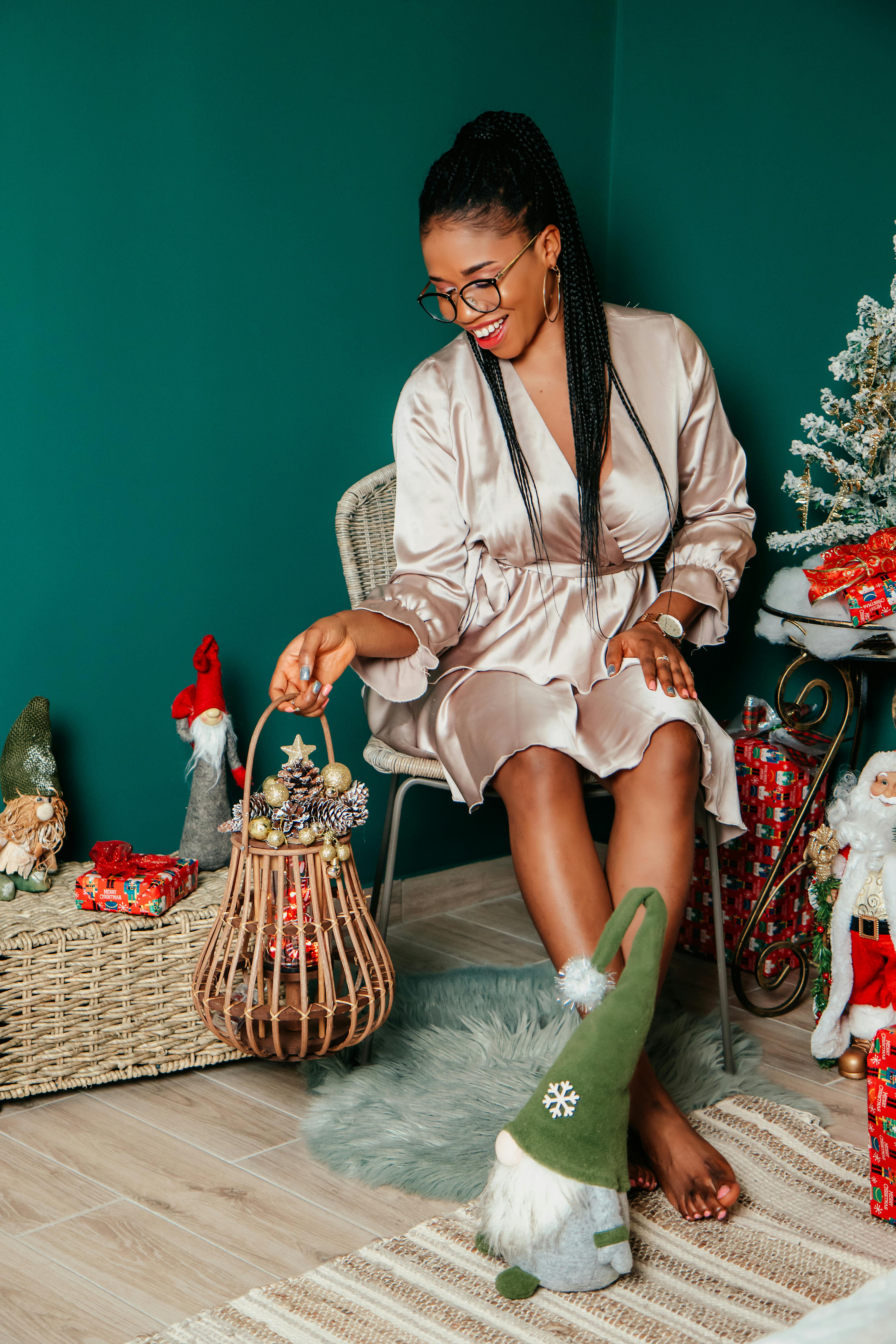 A stylish woman in a satin dress enjoys holiday decorations in a cozy room.