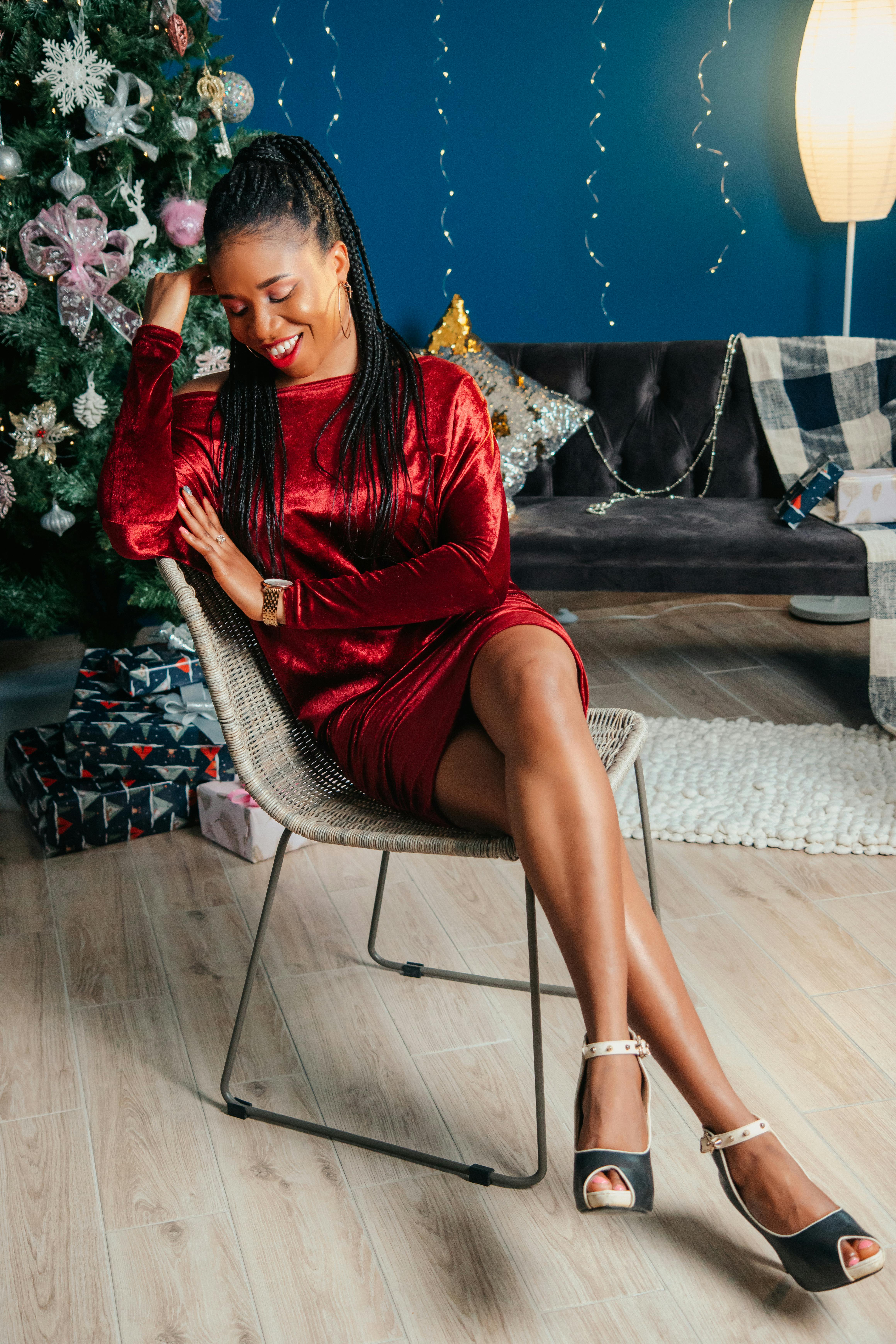Stylish woman in a red velvet dress posing by a Christmas tree inside a cozy living room.