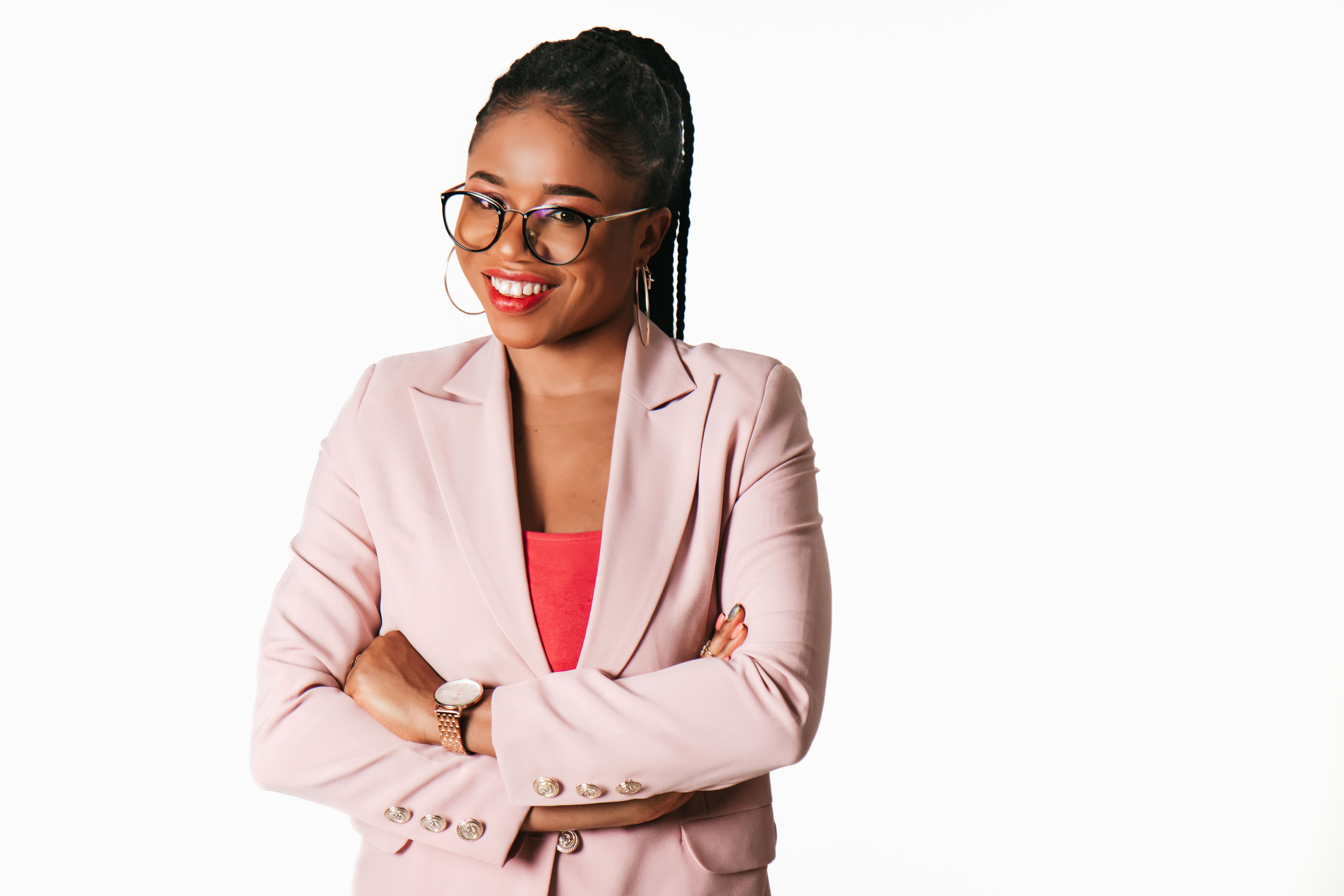 Confident woman with glasses and pink blazer posing with arms crossed against white background.