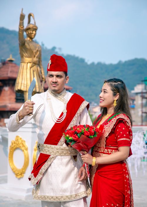 Free Couple in traditional clothing holding a knife and bouquet against urban backdrop. Stock Photo