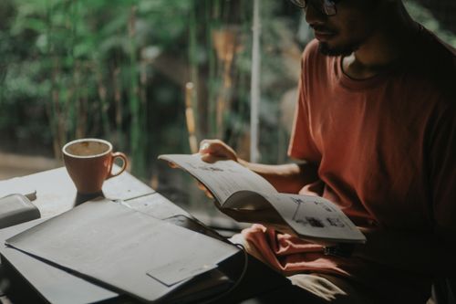 Free Man in a t-shirt reads a book indoors, enjoying a cup of coffee in a cozy atmosphere. Stock Photo