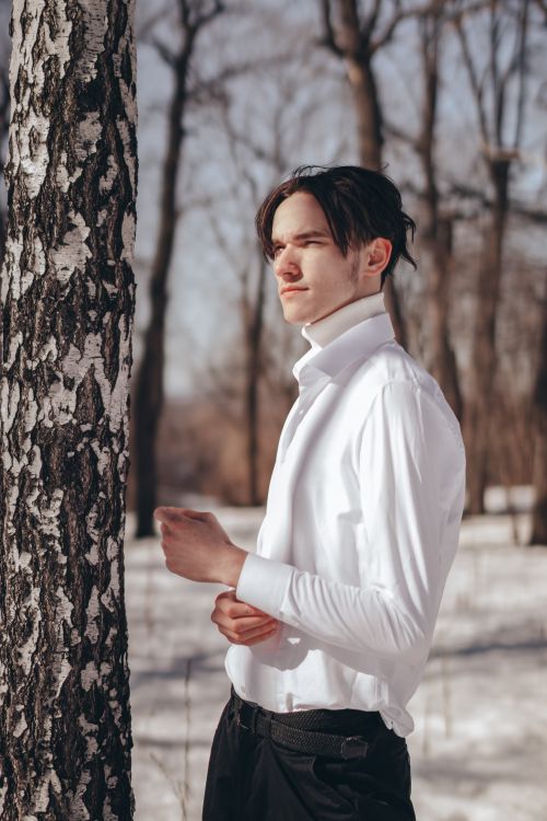 Free Stylish young man in a white shirt poses in a serene snowy forest, capturing winter fashion. Stock Photo