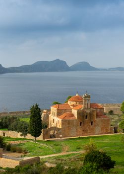A serene view of a historic stone church near the sea in Pylos, Greece.