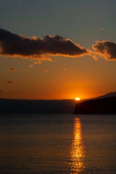 A tranquil seaside sunset with clouds reflecting on the calm water.