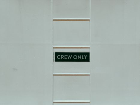 A minimalistic image featuring a 'Crew Only' sign on a ladder against a white wall.