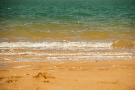 Calm beach scene with waves lapping against the sandy shore under a clear sky.