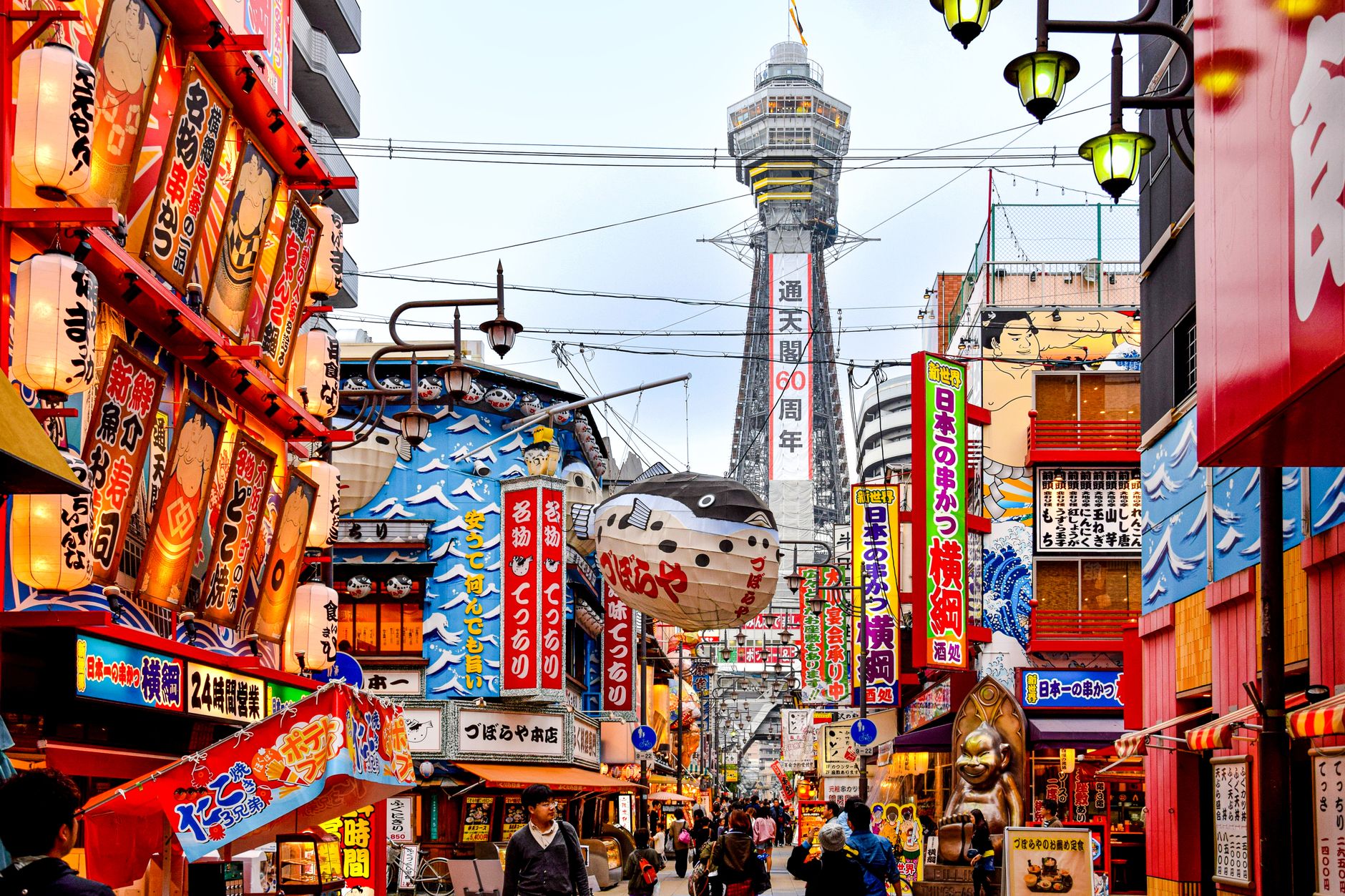 Discover the bustling streets of Osaka with a clear view of the iconic Tsūtenkaku Tower, showcasing vibrant urban culture.