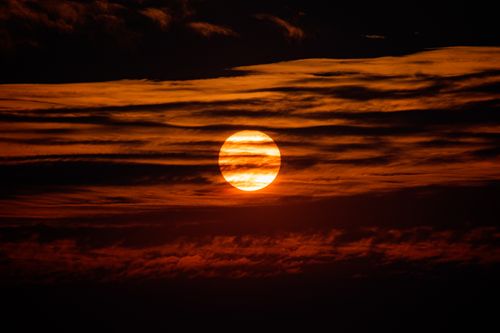 Free A striking sunset with the sun partially obscured by dark clouds, creating a fiery red sky. Stock Photo