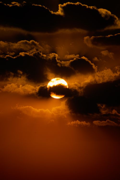 Free Captivating sunset with sun shrouded by dramatic clouds, creating a vibrant yellow sky. Stock Photo