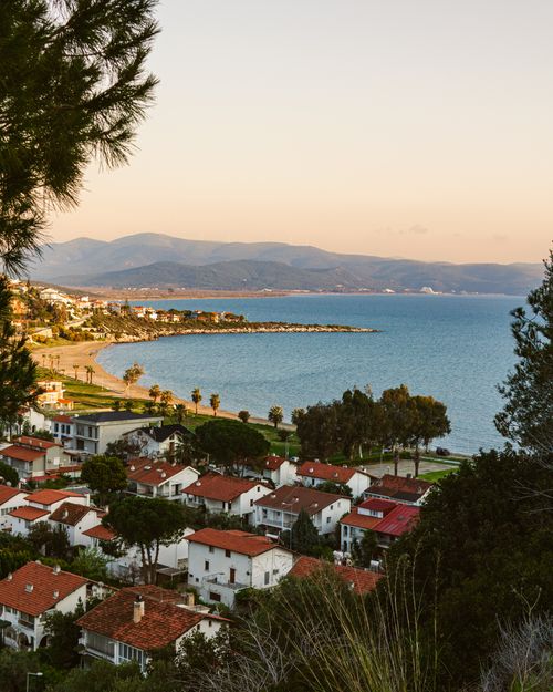 Free Charming coastal town with red rooftops by the sea at sunset, offering a picturesque bay view. Stock Photo