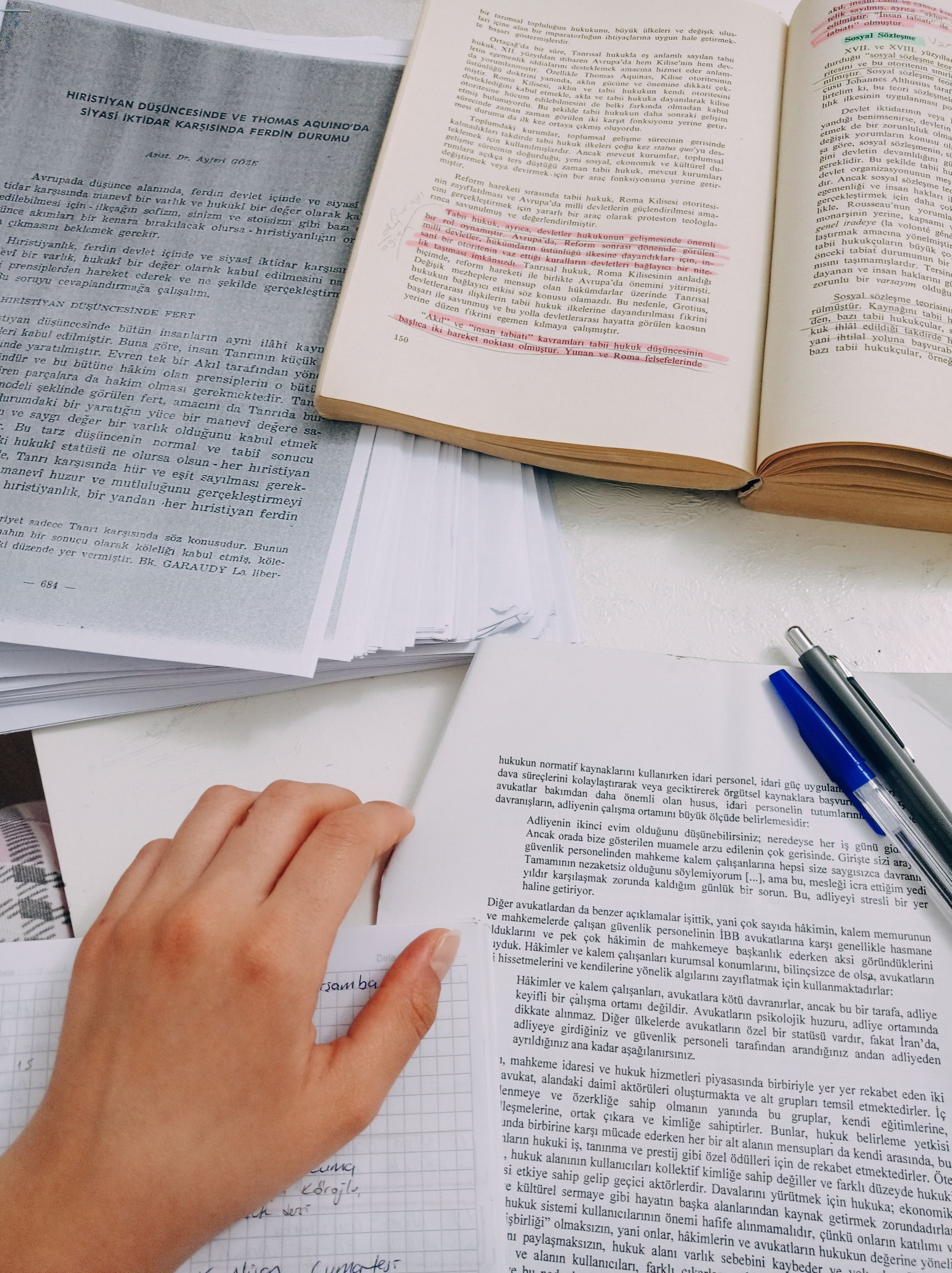 Hands reviewing open books and research notes at a study desk